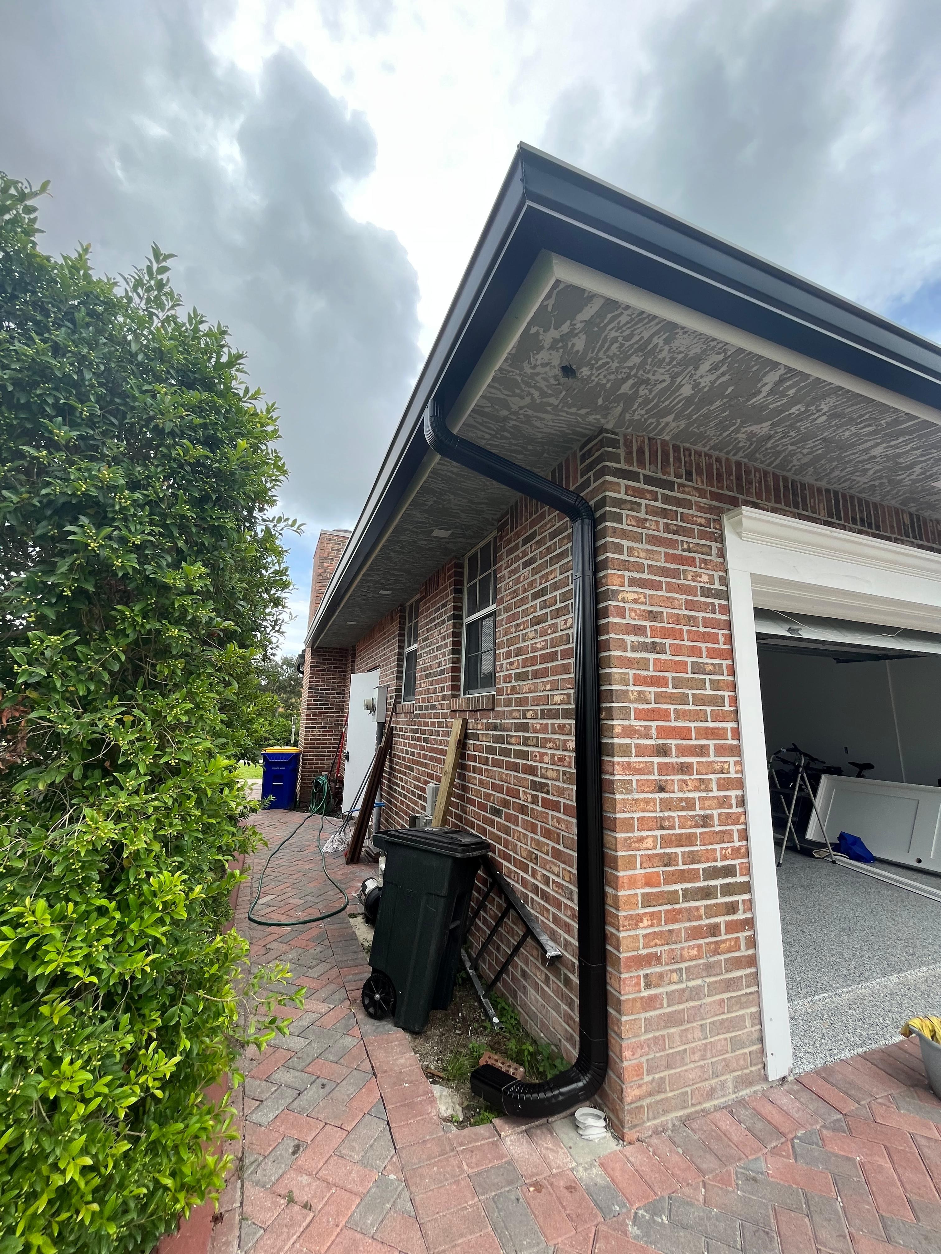 Black aluminum downspout running along the brick corner of a single-story garage