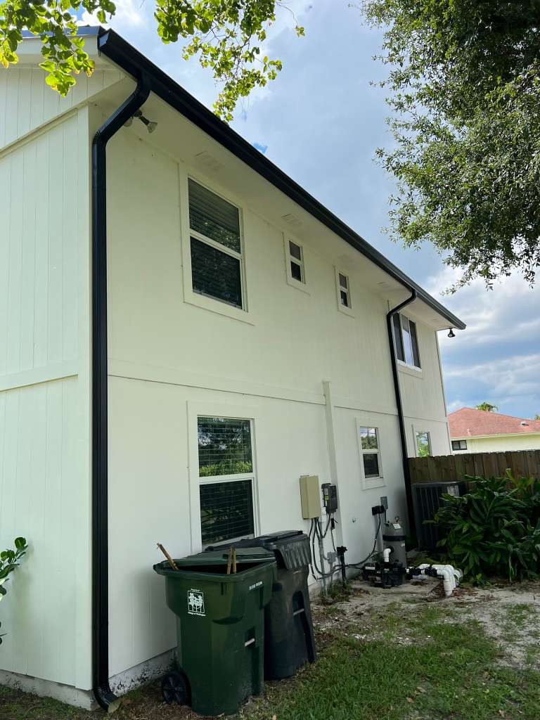 Black aluminum downspout running down the side of a two-story home with white siding