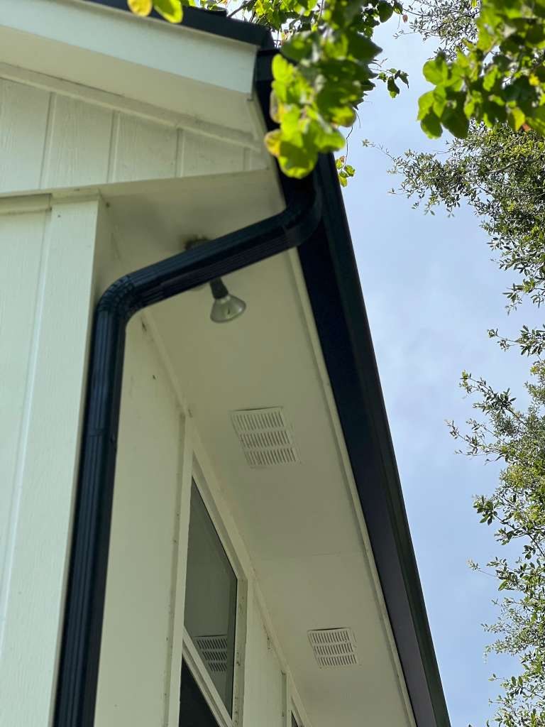 Black K-style aluminum gutter meeting at an outside corner with downspout running down the wall