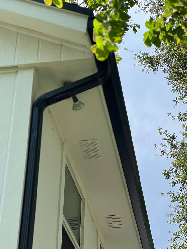 Black aluminum gutter and downspout meeting at the corner eave of a white board-and-batten home