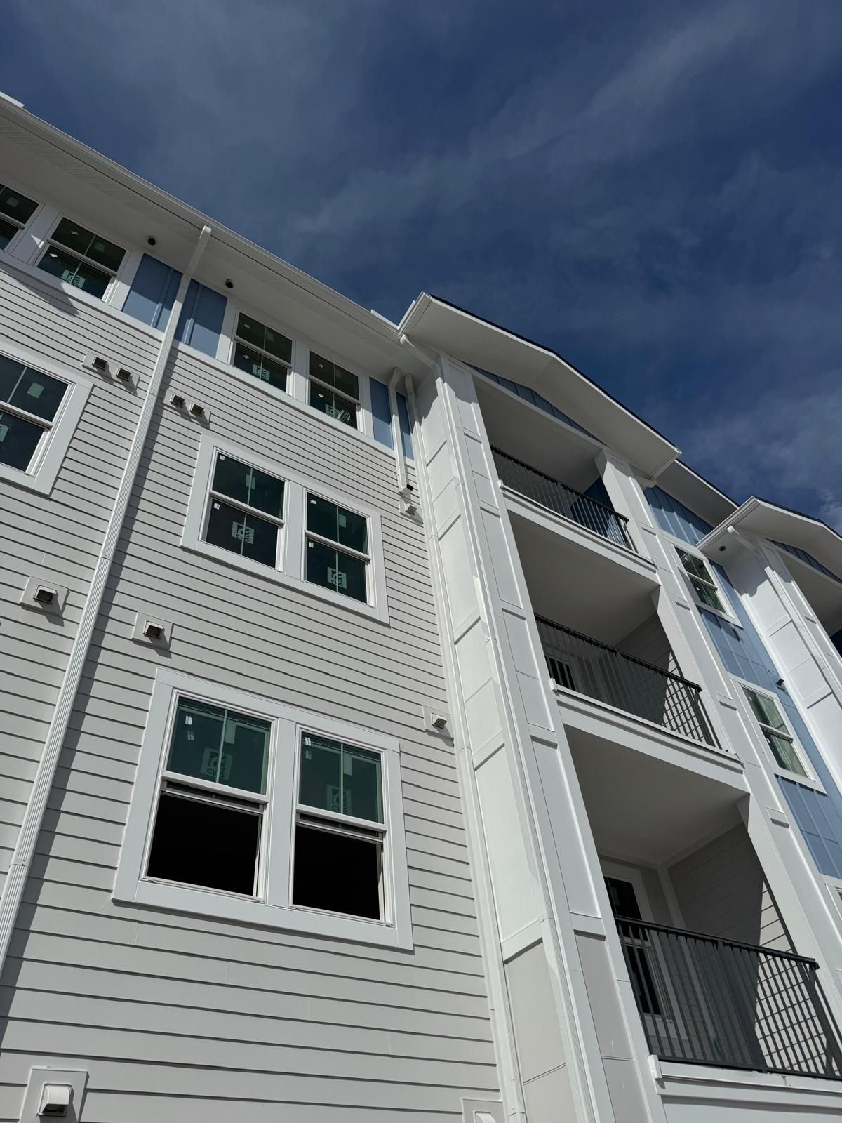 Looking up at a finished gutter and downspout system on a four-story white-siding apartment building