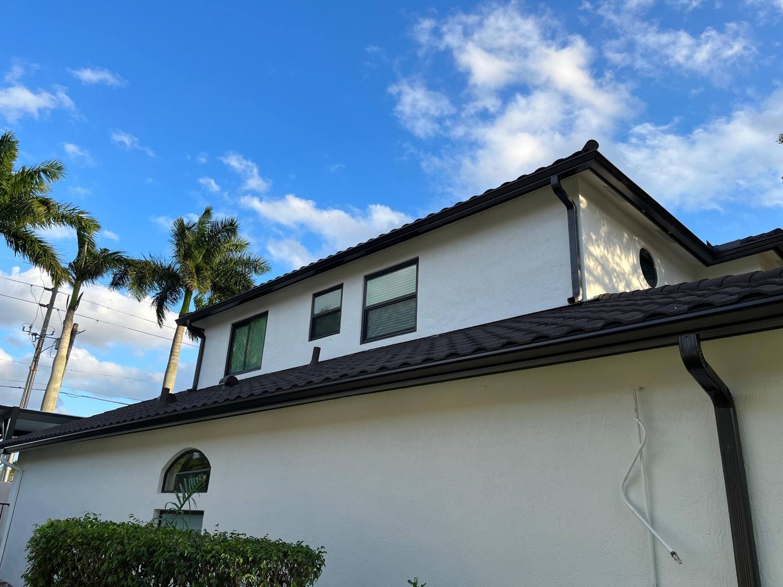 Dark bronze aluminum gutters and downspout on a two-story stucco home with a tile roof