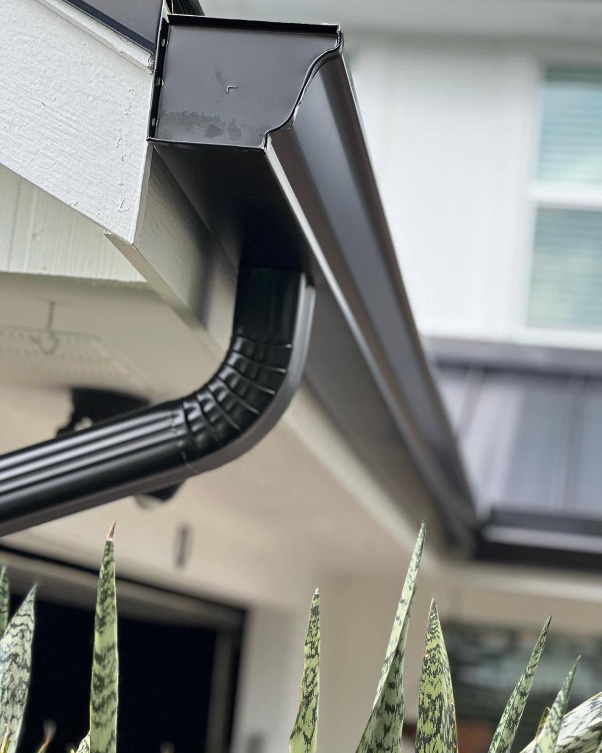 Dark brown K-style aluminum gutter at a corner end cap with a corrugated round downspout offset