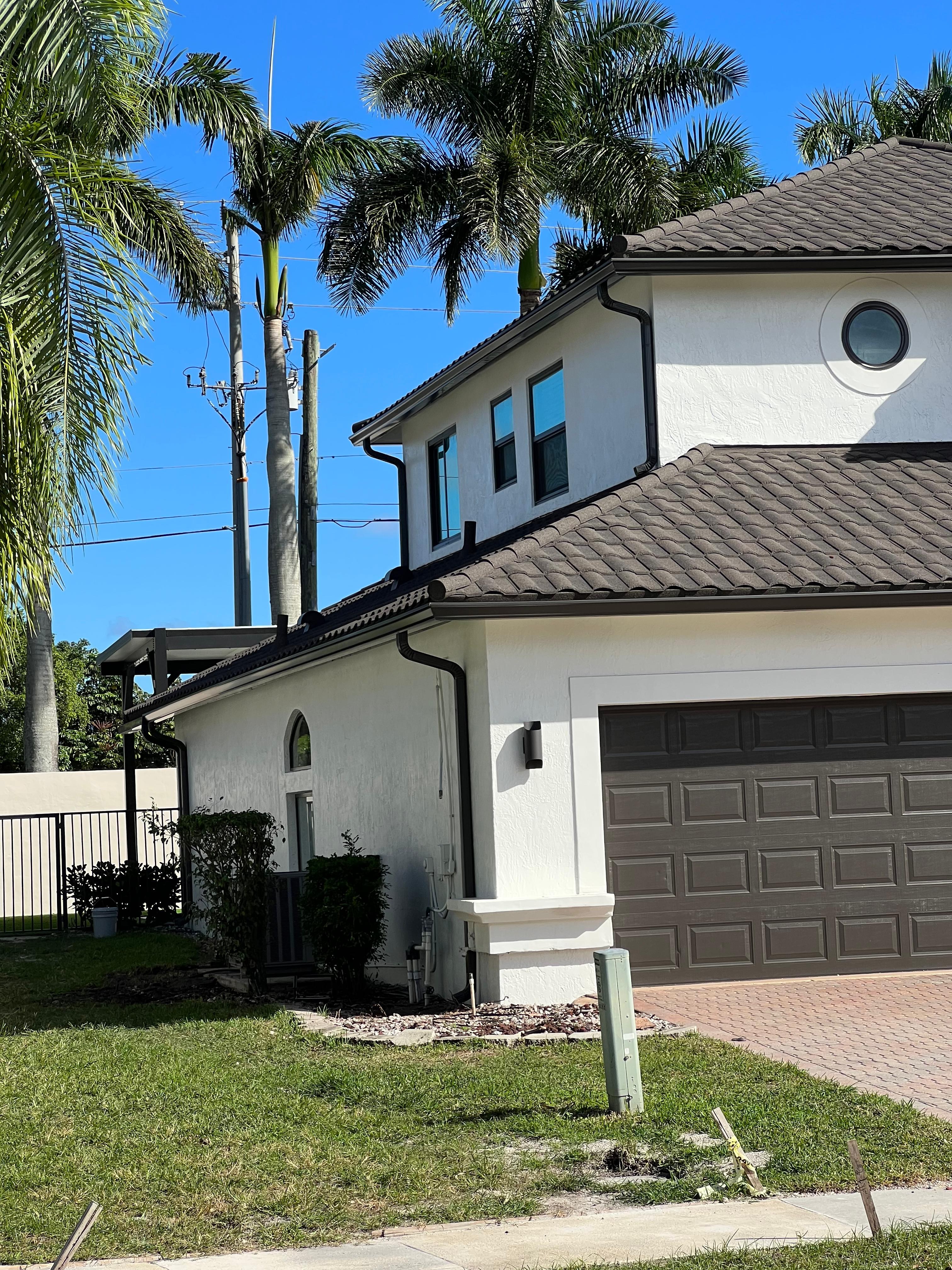Dark brown seamless aluminum gutters and downspouts on a two-story stucco home