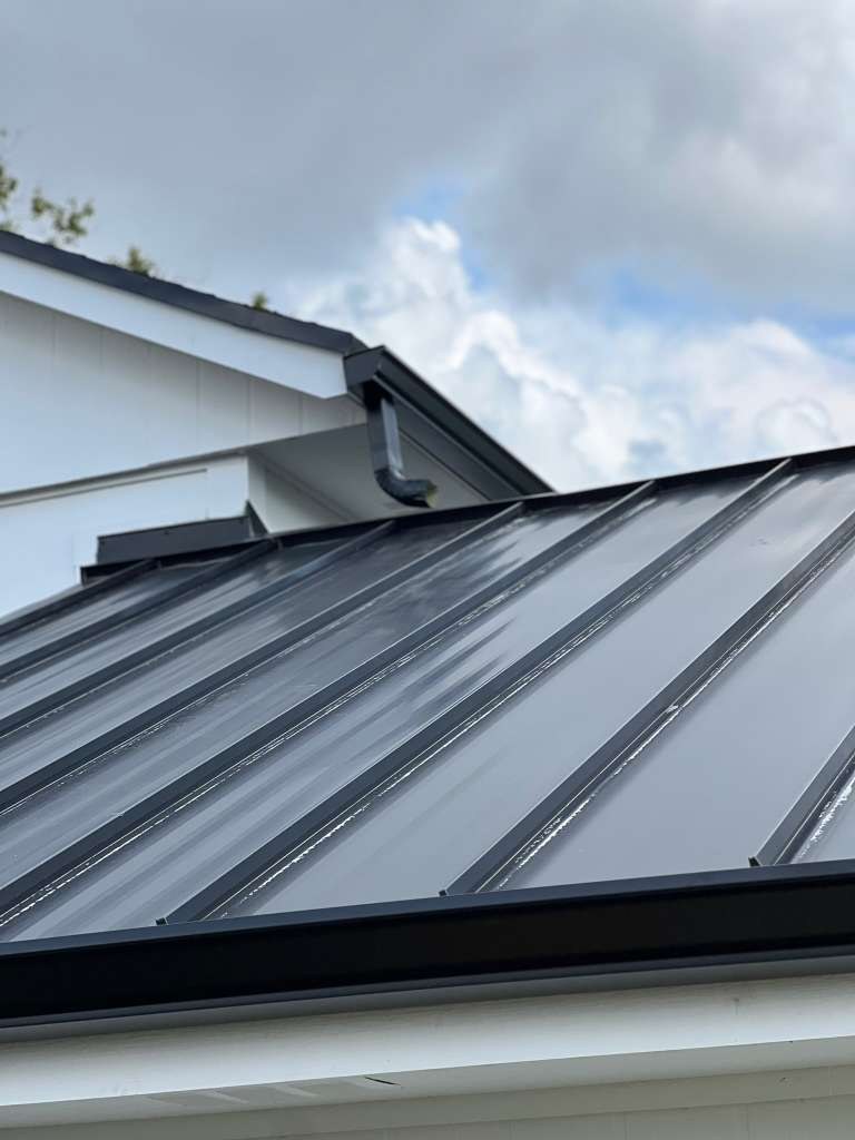 Dark seamless aluminum gutter installed along the eave of a home with a standing-seam metal roof