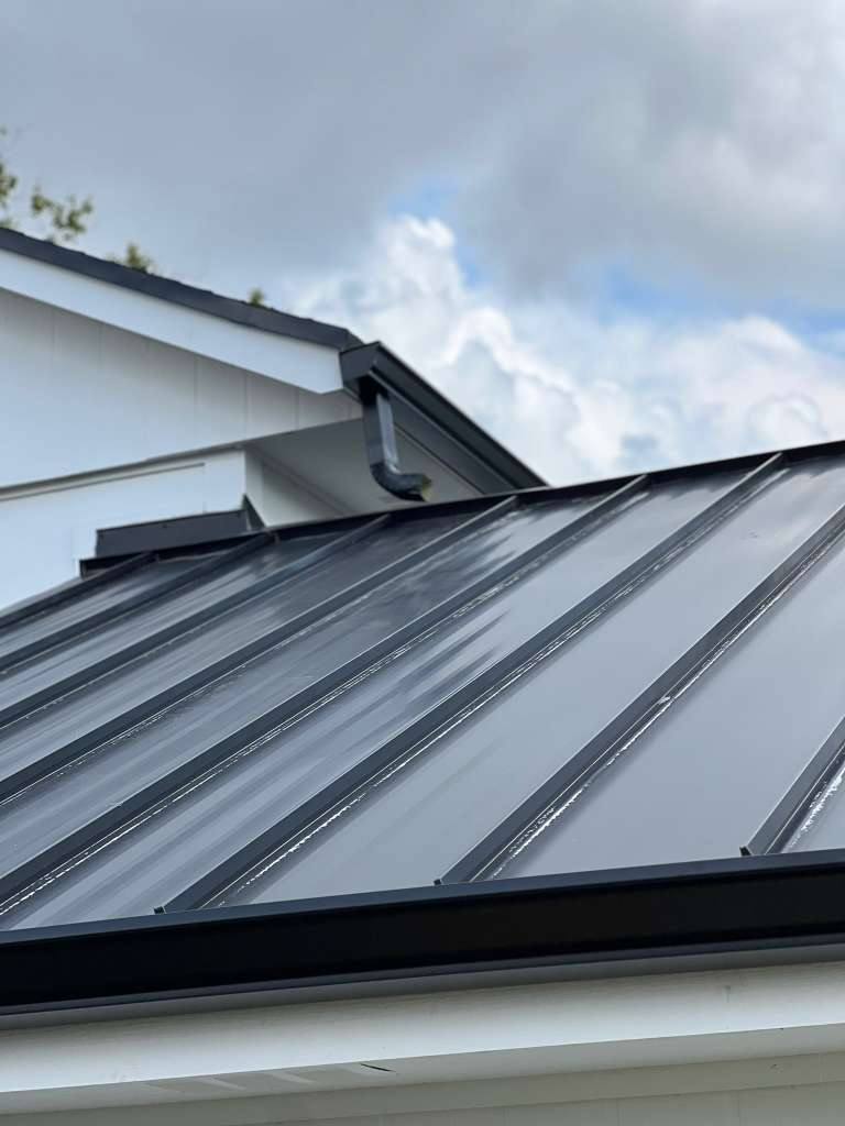 Dark charcoal standing-seam metal roof with matching dark aluminum gutters at the eave