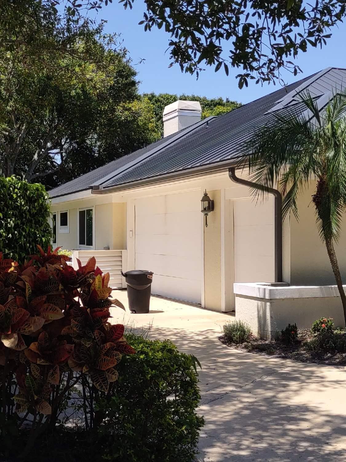 Single-story cream stucco home with a dark metal roof, two-car garage, and dark seamless aluminum gutters and downspouts