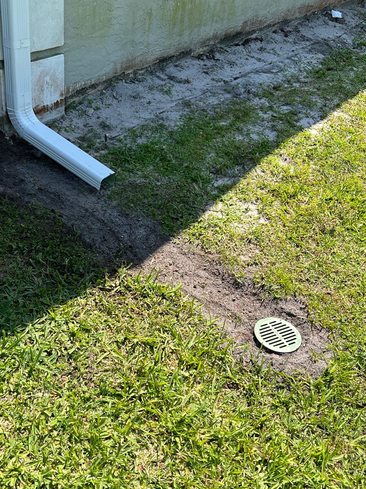 White downspout connected to an underground drain grate set in the lawn next to the foundation