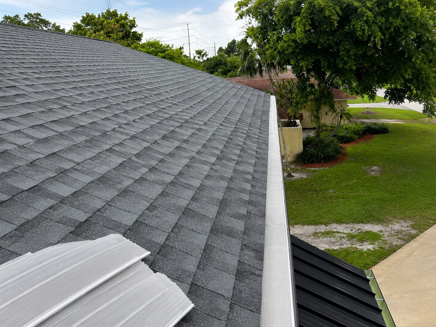 Perforated aluminum gutter guard installed along an aluminum gutter on a gray asphalt-shingle roof
