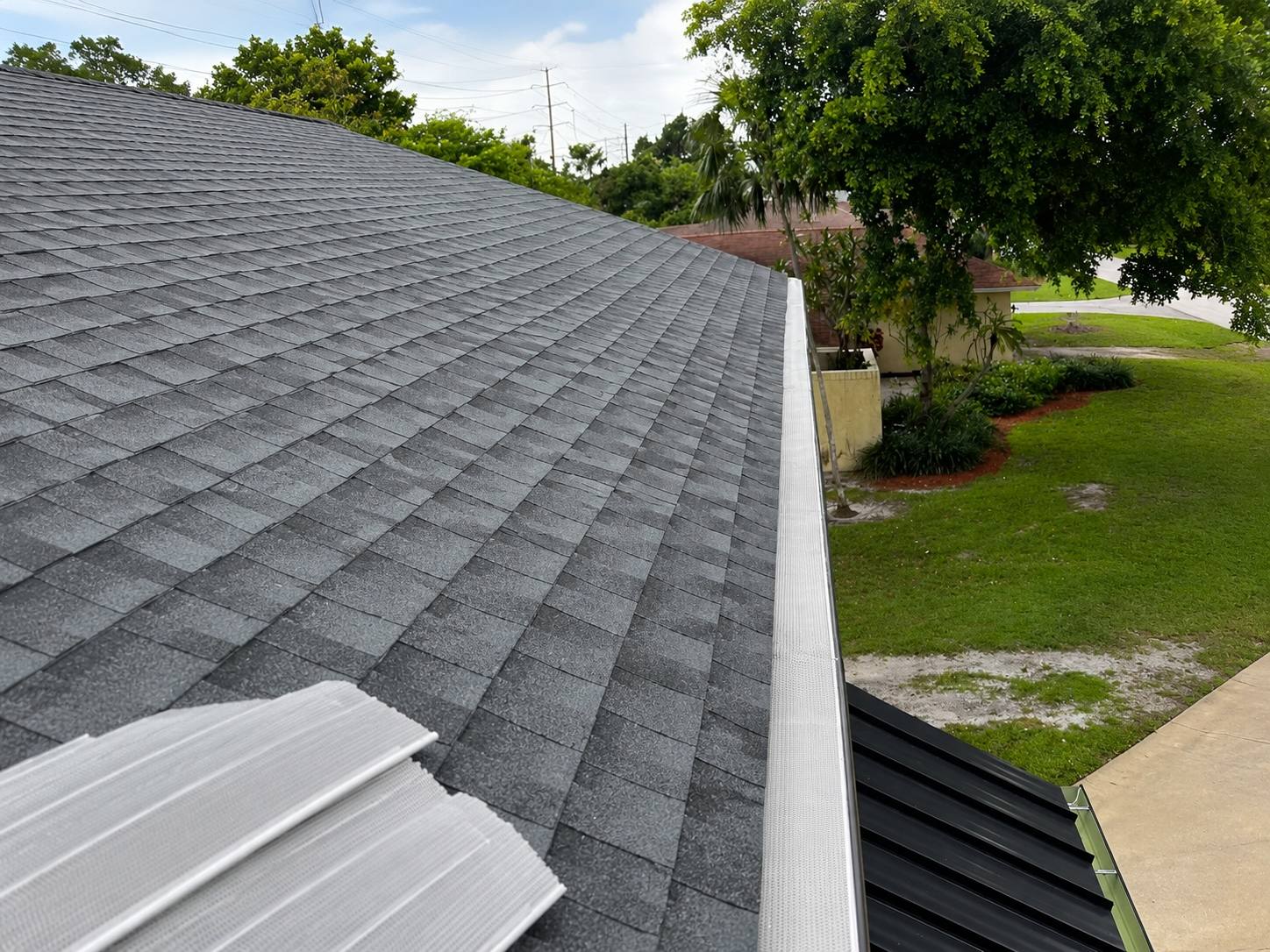 Gutter guard installed along an aluminum gutter on a gray asphalt-shingle roof
