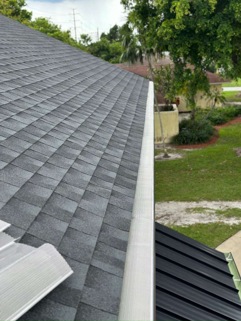 Perforated aluminum gutter guard installed on a gutter beneath an asphalt-shingle roof