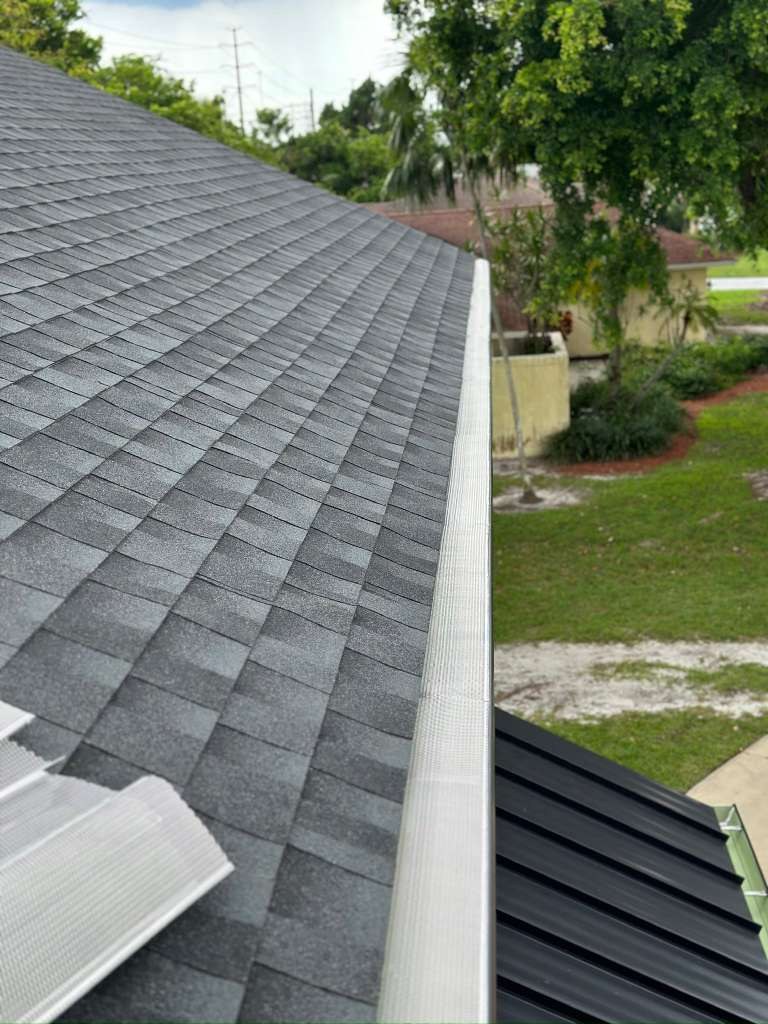 Perforated aluminum gutter guard installed inside a gutter on a home with a gray asphalt-shingle roof