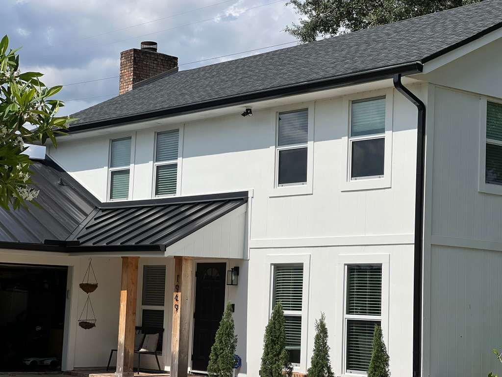 Black aluminum gutters and downspout installed on a white two-story farmhouse — the kind of system we walk before quoting a repair