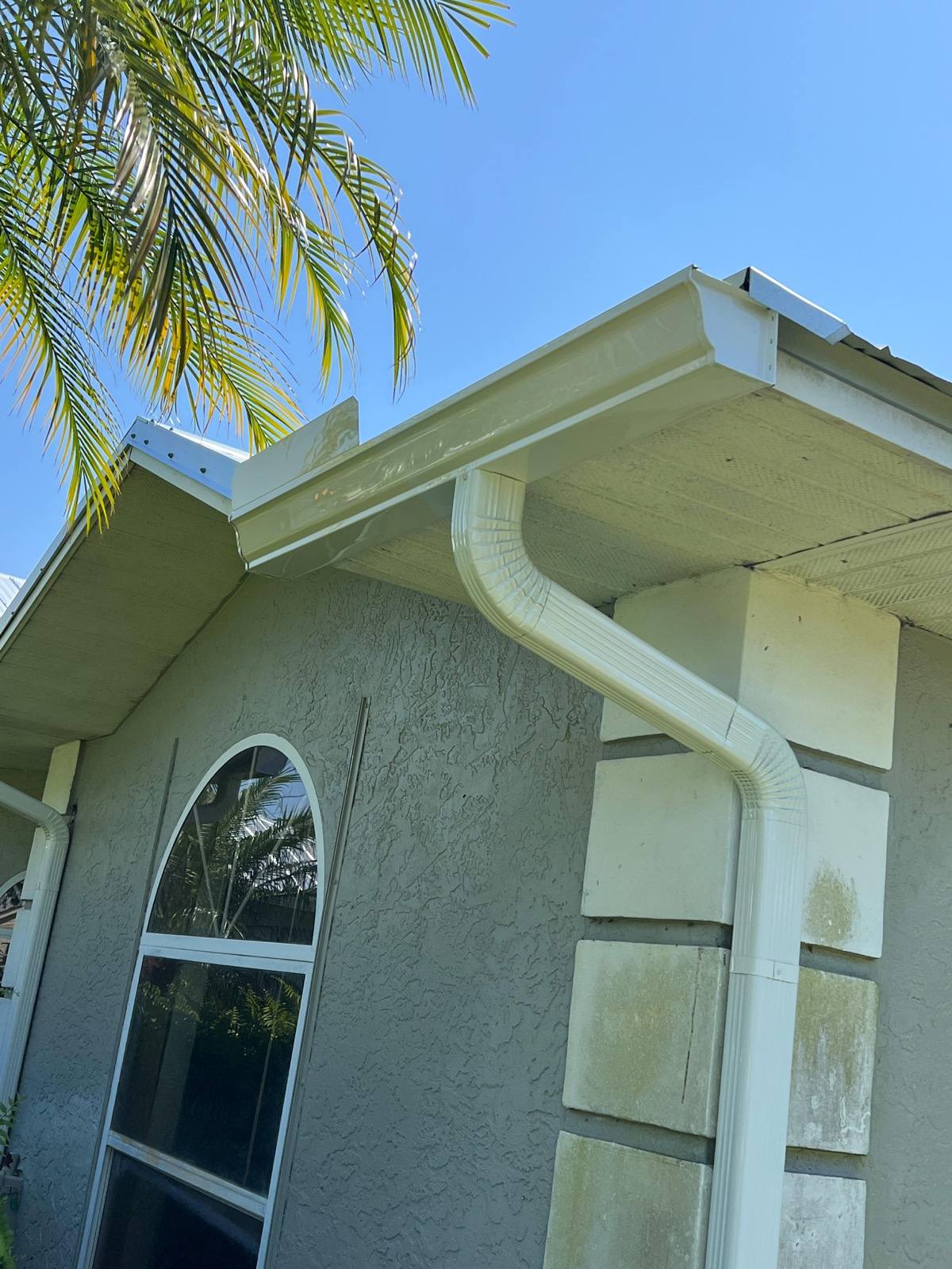 White aluminum K-style gutter and downspout at the corner of a tan stucco home with a palm tree overhead