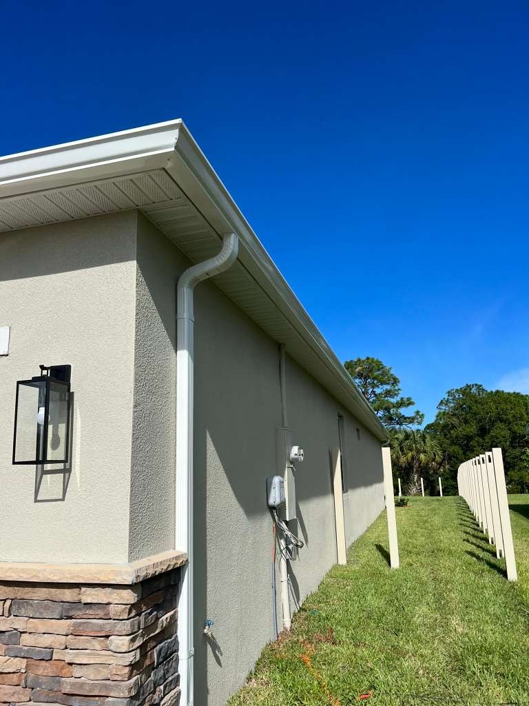 White K-style aluminum gutter and downspout on a single-story stucco home with a stone veneer base detail